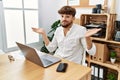 Young arab man working using computer laptop at the office clueless and confused expression with arms and hands raised Royalty Free Stock Photo