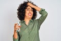 Young arab woman with curly hair holding glass of water over isolated white background stressed with hand on head, shocked with Royalty Free Stock Photo