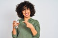 Young arab woman with curly hair holding glass of water over isolated white background very happy pointing with hand and finger Royalty Free Stock Photo