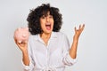 Young arab woman with curly hair holding piggy bank over isolated white background very happy and excited, winner expression Royalty Free Stock Photo