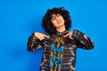 Young arab woman with curly hair wearing colorful shirt over isolated blue background looking confident with smile on face, Royalty Free Stock Photo