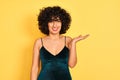 Young arab woman with curly hair wearing elegant dress over isolated yellow background smiling cheerful presenting and pointing Royalty Free Stock Photo