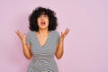 Young arab woman with curly hair wearing striped dress over isolated pink background crazy and mad shouting and yelling with Royalty Free Stock Photo