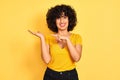 Young arab woman with curly hair wearing t-shirt standing over isolated yellow background amazed and smiling to the camera while Royalty Free Stock Photo