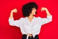 Young arab woman with curly hair wearing white casual shirt over isolated red background showing arms muscles smiling proud Royalty Free Stock Photo