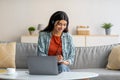 Young Arab woman in headphones using laptop, working or studying online from home, taking notes during business meeting Royalty Free Stock Photo