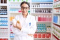 Young arab woman pharmacist holding pills bottles standing with arms crossed gesture at pharmacy Royalty Free Stock Photo