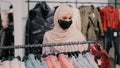 Young arab woman shopper in medical protective mask chooses clothes in clothing store retail sales discount purchase