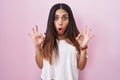 Young arab woman standing over pink background looking surprised and shocked doing ok approval symbol with fingers Royalty Free Stock Photo