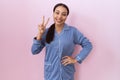 Young arab woman wearing blue pajama smiling with happy face winking at the camera doing victory sign with fingers