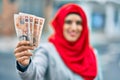 Young arab woman wearing hijab holding uk pounds at the city