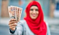 Young arab woman wearing hijab holding uk pounds at the city