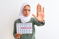 Young Arab woman wearing hijab showing menstruation calendar over isolated background with open hand doing stop sign with serious