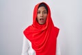 Young arab woman wearing traditional islamic hijab scarf in shock face, looking skeptical and sarcastic, surprised with open mouth