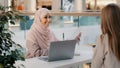 Young arab woman consultant sales agent bank worker sitting at office desk advises unrecognizable girl client offers to Royalty Free Stock Photo