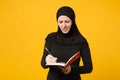 Young arabian muslim woman in hijab black clothes hold notebook, writing, prepare to exam isolated on yellow wall Royalty Free Stock Photo