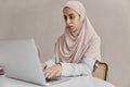 Young arabian woman in hijab sitting on her worklplace and working on laptop on light background. Royalty Free Stock Photo