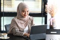 Young Arabic female entrepreneur wearing a hijab is sitting in office and working online with tablet.