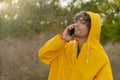 Young arabic man wearing a yellow raincoat calling on phone during the rain in the park. Guy outdoors call in taxi Royalty Free Stock Photo