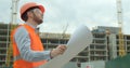 Young architect or builder With Hard Hat Holding Blueprint In His Hands in front of building under construction. Close Royalty Free Stock Photo