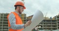 Young architect or builder With Hard Hat Holding Blueprint In His Hands in front of building under construction. Close Royalty Free Stock Photo