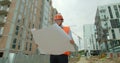 Young architect or builder With Hard Hat Holding Blueprint In His Hands in front of building under construction. Close Royalty Free Stock Photo