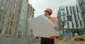 Young architect or builder With Hard Hat Holding Blueprint In His Hands in front of building under construction. Close Royalty Free Stock Photo
