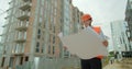 Young architect or builder With Hard Hat Holding Blueprint In His Hands in front of building under construction. Close Royalty Free Stock Photo