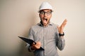 Young architect inspector man wearing builder safety helmet and using clipboard very happy and excited, winner expression Royalty Free Stock Photo