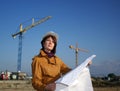 Young architect looking at blueprint against crane