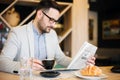 Young architect reading newspapers and drinking coffee in a modern cafe. Work anywhere concept