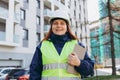 Young architect woman in white hardhat and safety vest using digital tablet outdoors. Female construction engineer Royalty Free Stock Photo