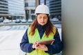 Young architect woman in white hardhat and safety vest using digital tablet outdoors. Female construction engineer Royalty Free Stock Photo