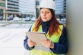 Young architect woman in white hardhat and safety vest using digital tablet outdoors. Female construction engineer Royalty Free Stock Photo