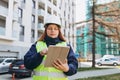 Young architect woman in white hardhat and safety vest using digital tablet outdoors. Female construction engineer Royalty Free Stock Photo