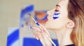 Young artist painting. Girl painting a picture in home studio. Model painting brush on easel. Sensual woman with paint on the face Royalty Free Stock Photo