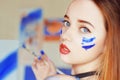 Young artist painting. Girl painting a picture in home studio. Model painting brush on easel. Sensual woman with paint on the face Royalty Free Stock Photo