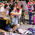 A young artist paints a picture of multicolored spray paint at night in front of everybody. A young guy in a respirator.