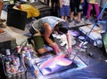 A young artist paints a picture of multicolored spray paint at night in front of everybody. A young guy in a respirator.