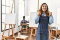 Young artist woman at art studio excited for success with arms raised and eyes closed celebrating victory smiling Royalty Free Stock Photo