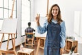 Young artist woman at art studio showing and pointing up with fingers number two while smiling confident and happy Royalty Free Stock Photo