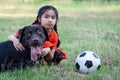 A young Asain girl playing football with her big black dog outside the grass ground in the yard in the evening