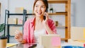 Young Asia businesswoman using mobile phone call receiving purchase order and check product on stock, work at home office. Small