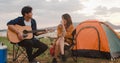 Young asia campers couple playing guitar serenading each other near beach. Male and female travel happy romantic moment when Royalty Free Stock Photo