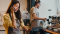 Young Asia female barista taking order by mobile phone and digital tablet standing behind bar counter while talking with customer Royalty Free Stock Photo