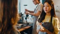 Young Asia female barista waiter taking order from customer standing behind bar counter while talking with customer making note on Royalty Free Stock Photo