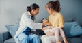 Young Asia female pediatrician hold stethoscope exam little girl patient visit doctor with mother sit on couch in living room at