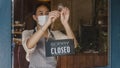 Young Asia girl wear face mask turning a sign from closed to open sign on door looking outside waiting for clients after lockdown Royalty Free Stock Photo