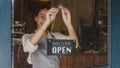 Young Asia manager girl changing a sign from closed to open sign on door cafe looking outside waiting for clients after lockdown. Royalty Free Stock Photo