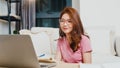 Young Asia teen girl student wears headphones distance learning lesson with online teacher on laptop in living room from home. Royalty Free Stock Photo